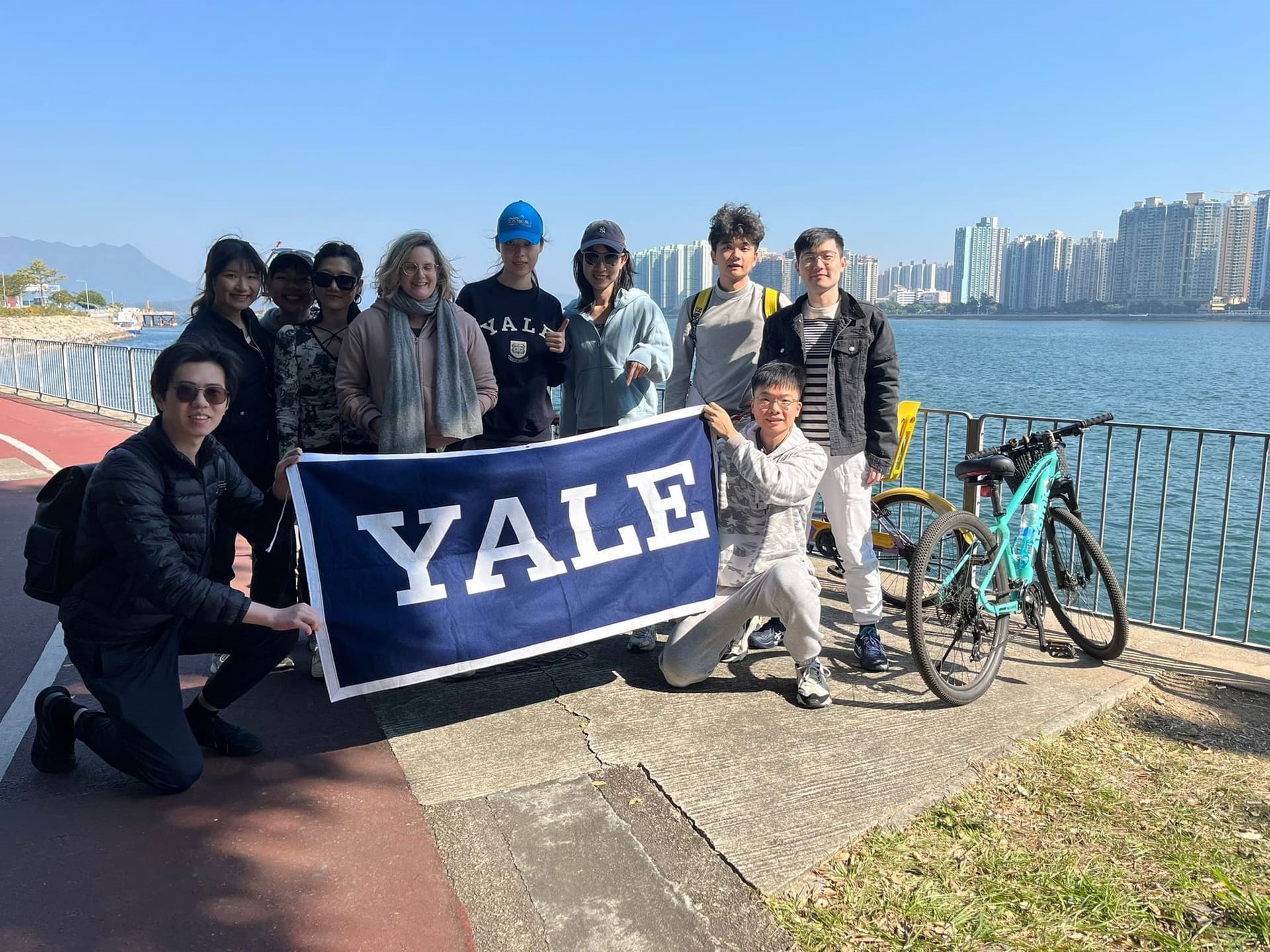 Club members with a Yale banner and bicycles beside the harbour