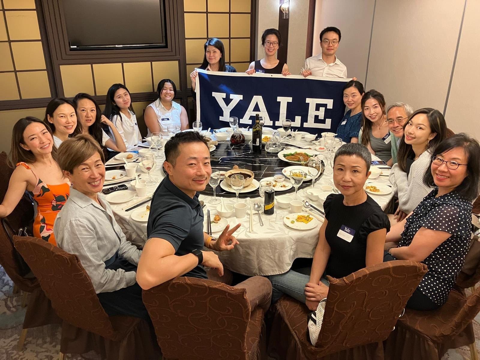 The Yale Club of Hong Kong Foodies group around a banquet table with a Yale banner