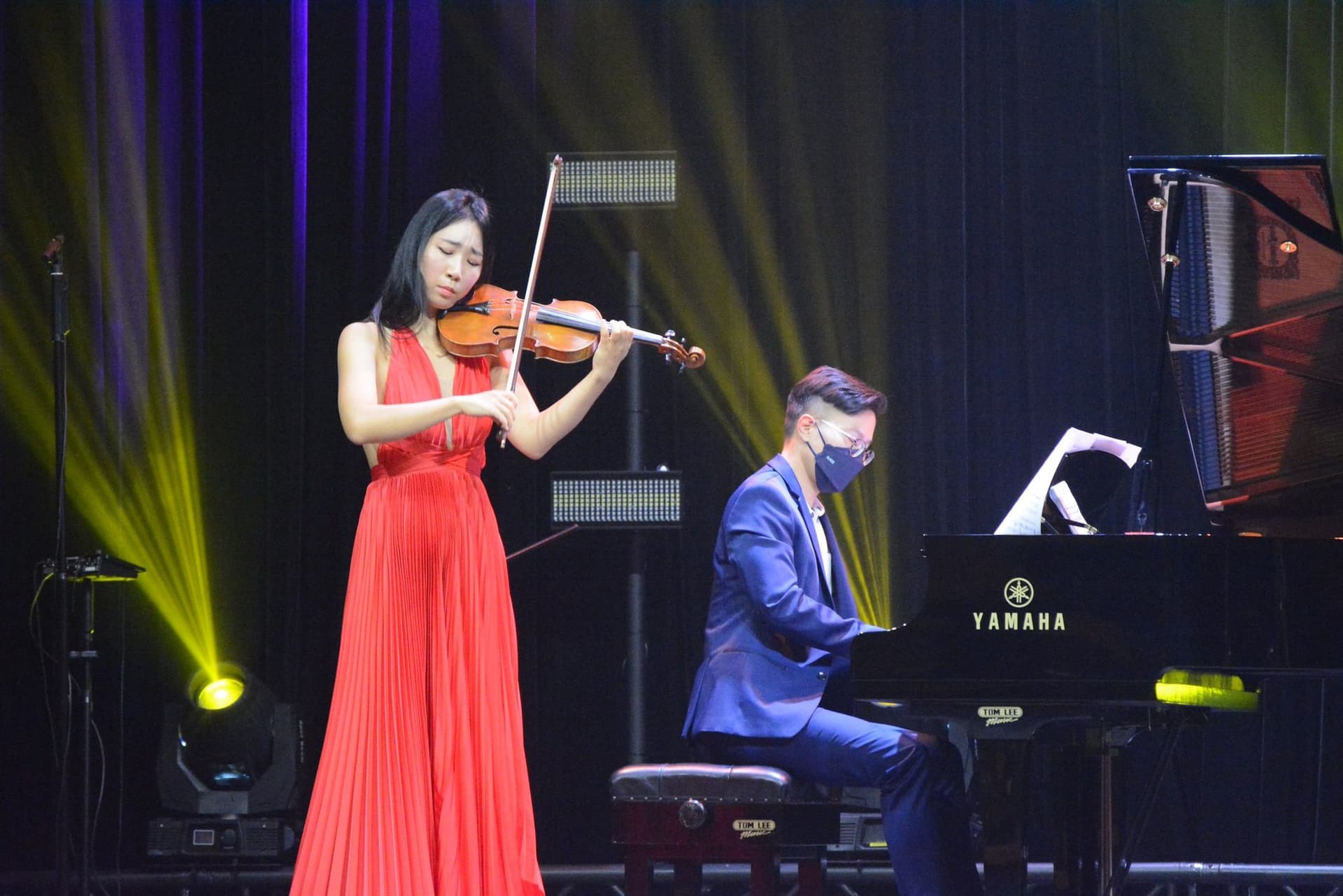A violinist and pianist performing on a lit stage