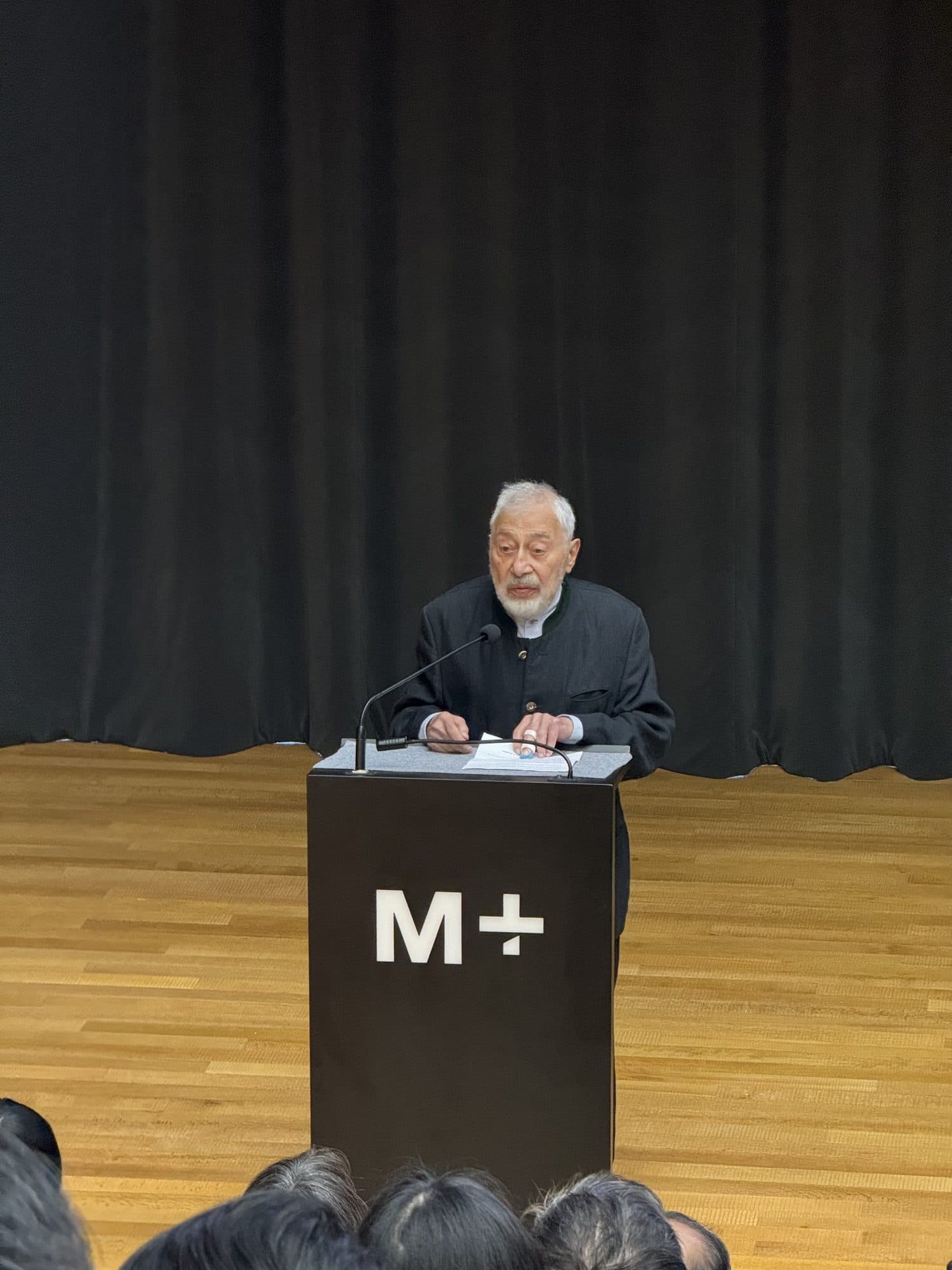Henry Steiner speaking at a podium at the M+ museum in Hong Kong